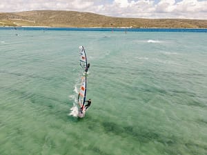Instruktor windsurfingu płynie za kursantem na płytkiej lagunie w Alacati