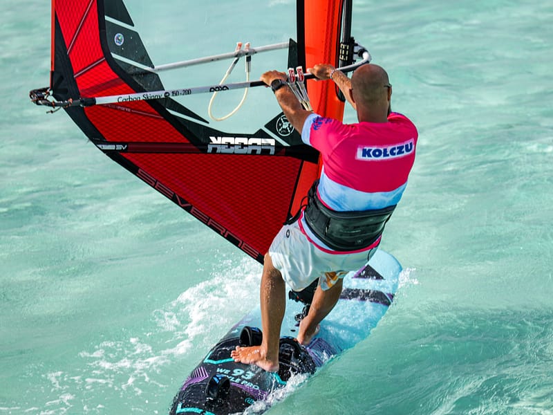 Instruktor windsurfingu Wavecamp płynie na desce windsurfingowej w koszulce firmowej na karaibach